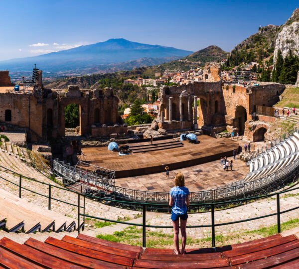 Panoramic photo of a tourist visiting Teatro Greco aka Taormina Greek Theatre, with Mount Etna Volca
