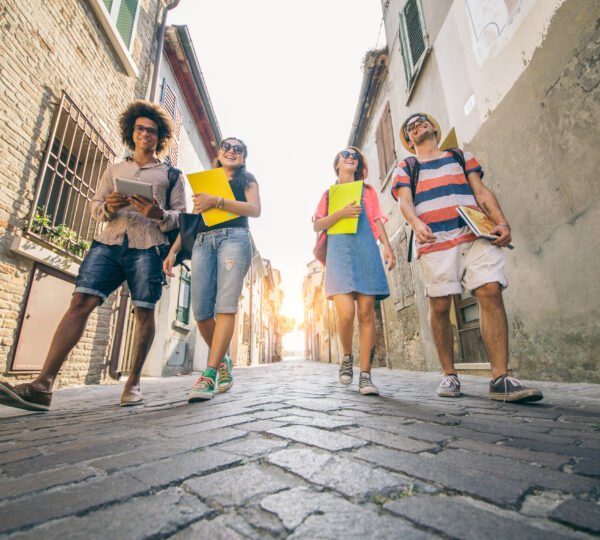 Group of multi-ethnic students talking and laughing while going to university - Four happy friends walking outdoors
