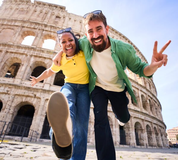 Happy multi-ethnic couple of tourists visiting the colosseum in rome, italy, joyfully making victory signs while smiling and enjoying their memorable adventure under the sunny sky